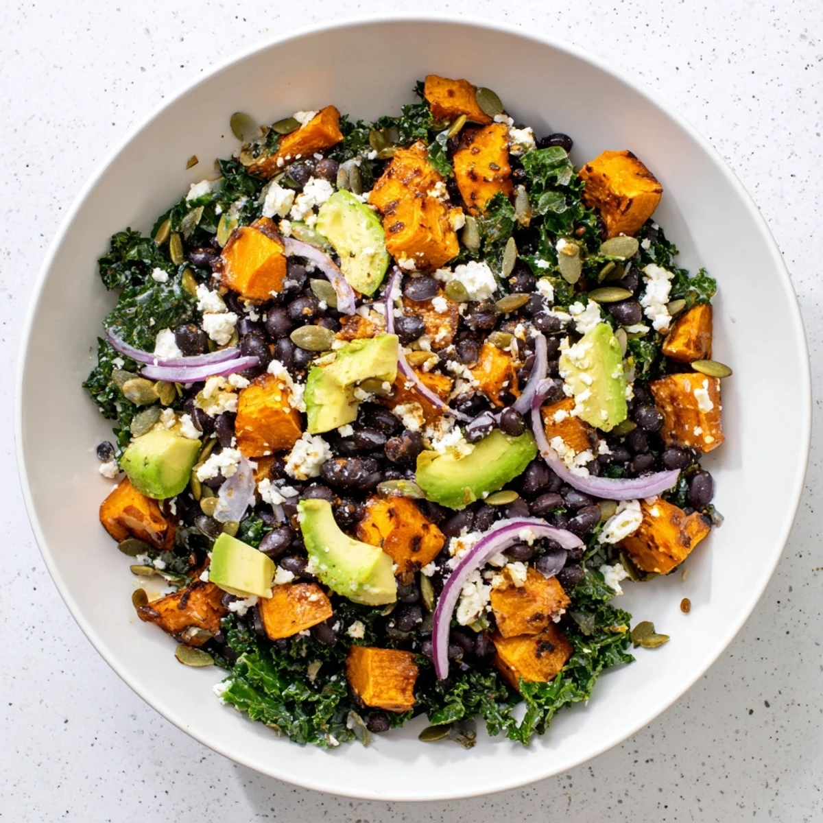 Close-up of hearty massaged kale salad with creamy avocado, sweet potato, and black beans ready to enjoy.