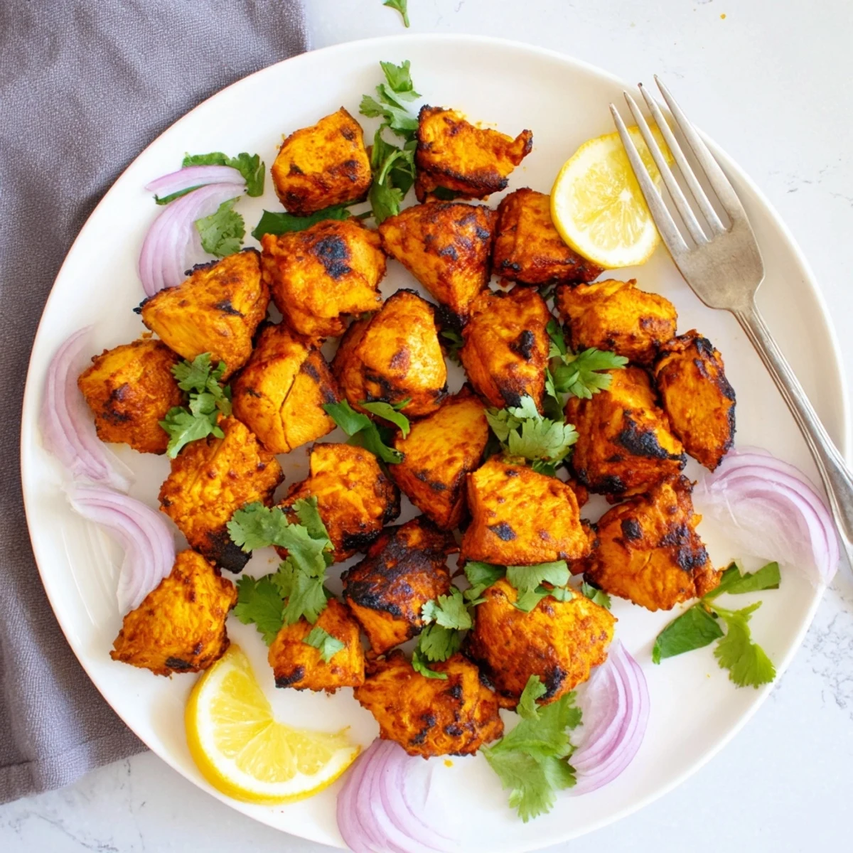 Golden-brown Indian Tikka Spiced Chicken pieces roasted on a wire rack, garnished with fresh cilantro and lemon wedges.  