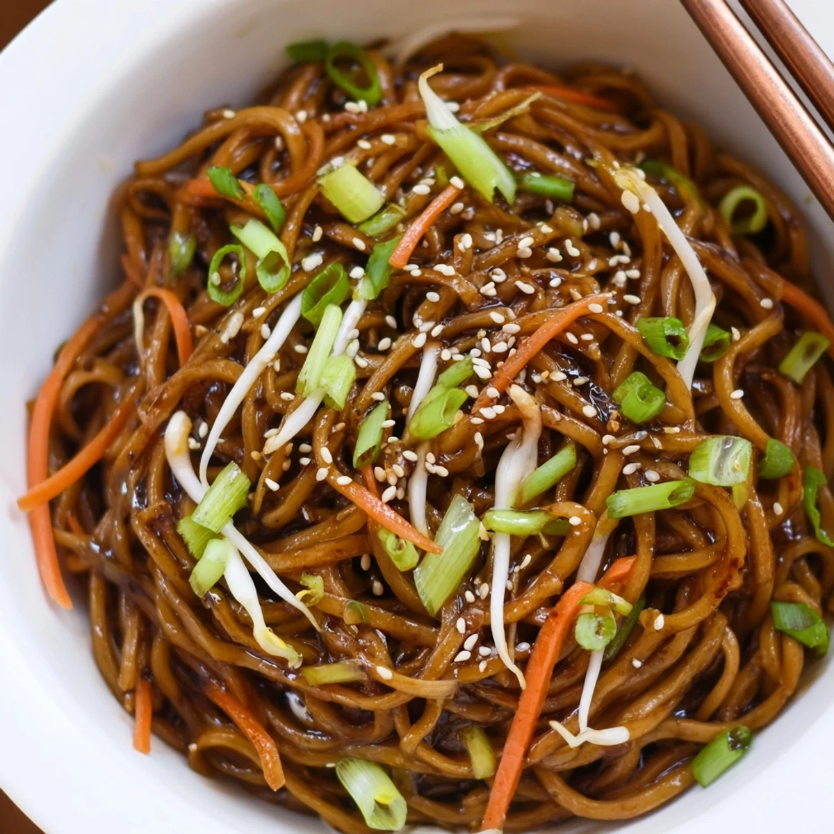 A close-up of glossy Asian Garlic Noodle Bowl tossed in rich garlic-butter sauce with colorful vegetable toppings.