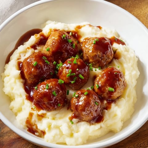 Juicy BBQ meatballs glistening in a rich sauce atop a fluffy bed of mashed potatoes.