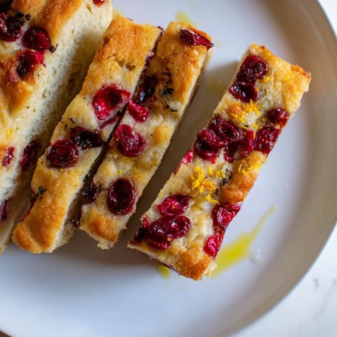 Golden-crusted cranberry orange no-knead focaccia, bubbling with fresh cranberries and zesty orange slices.