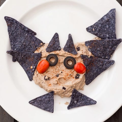 Creamy Spooky Bat Bean Dip Platter, artfully shaped with olive eyes and colorful veggies, ready to devour.