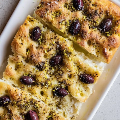 Golden brown Zaatar Olive Focaccia, dotted with olives, is ready to be sliced, perfect for sharing.