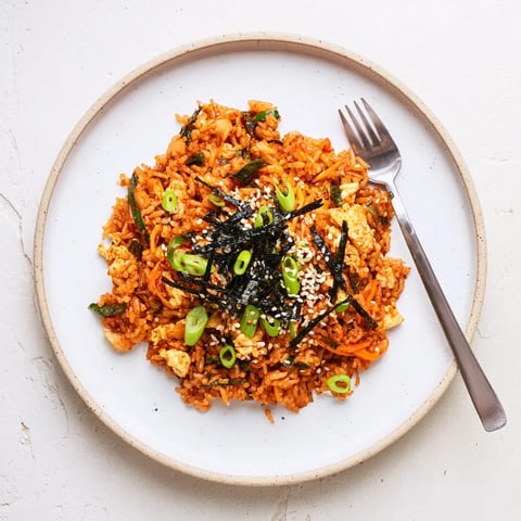 A steaming skillet of Spicy Kimchi Fried Rice with glossy grains, scrambled eggs, and fresh green onion garnish.  
