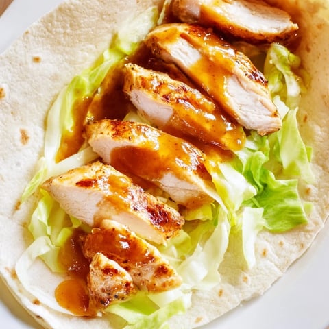 Golden-brown honey mustard chicken wrap filled with crisp romaine lettuce and sliced tomato on a rustic wooden board.