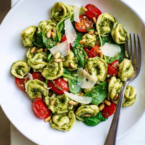 A vibrant bowl of Pesto Tortellini Salad features tender cheese tortellini tossed with bright basil pesto and halved cherry tomatoes.
