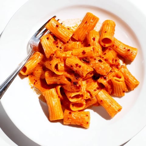 Creamy spicy rigatoni pasta coated in a rich tomato cream sauce, garnished with fresh basil and Parmesan for a comforting Italian-American dinner.