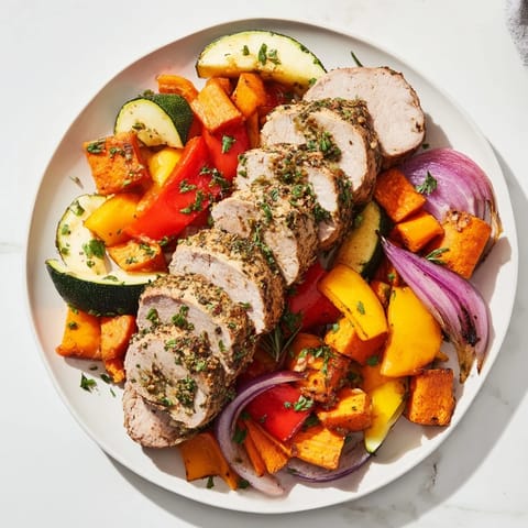 Juicy roasted garlic pork tenderloin alongside colorful roasted bell peppers and zucchini, ready to serve.