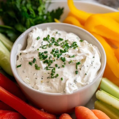 A spread of colorful veggie sticks surround a bowl of creamy, homemade cream cheese and ranch dip.