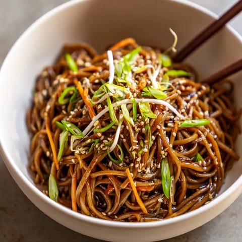 Steaming Asian Garlic Noodle Bowl garnished with fresh green onions and toasted sesame seeds on a white plate.