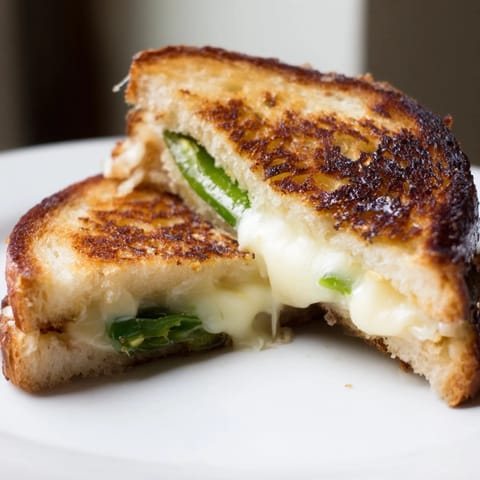 Golden-brown Jalapeño Havarti Grilled Cheese halves sit beside a small bowl of creamy tomato soup, perfect for a cozy lunch or dinner.