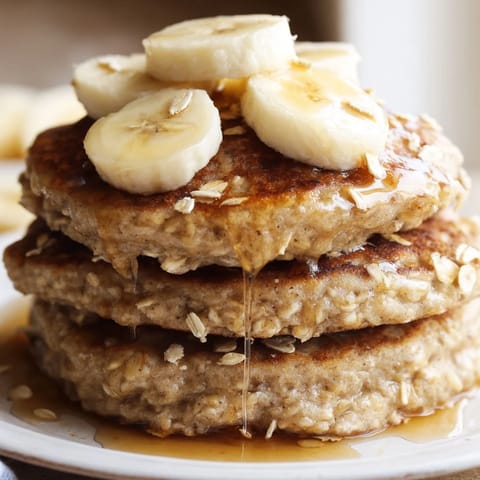 Freshly cooked Banana Oat Pancakes on a rustic plate, served alongside creamy yogurt and a sprinkle of cinnamon.  