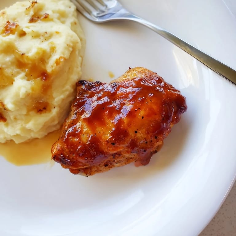 Savory honey BBQ chicken thighs next to velvety garlic mashed potatoes in a rustic setting.